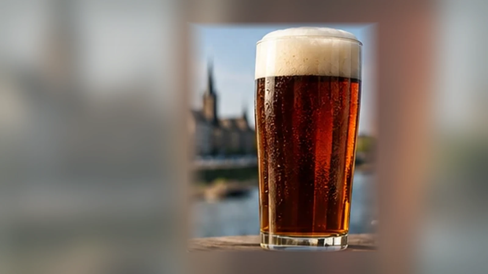 Klares kupferfarbenes Altbier in einem schlanken neutralen Glas vor unscharfer Düsseldorfer Stadtkulisse
